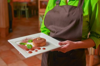 Garson, fındıklı çikolatalı tatlı ve mavi tabakta karamel sosu servis ediyor. Lezzetli tatlı. Restoranda yemek yiyorum. İşteki üniformalı garson. Restoran servisi..