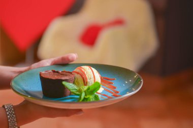 Garson, vanilyalı dondurma ve çikolatalı karamel soslu çikolatalı brownie servis ediyor. Lezzetli tatlı. Restoranda yemek yiyorum. İşteki üniformalı garson. Restoran servisi..