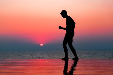 Havuzda gün batımının tadını çıkaran genç bir adam. Batan güneşin üzerinde insan silueti. Denge. Deniz Burnu. Uzay afişini kopyala. Gökyüzü arkaplanı.