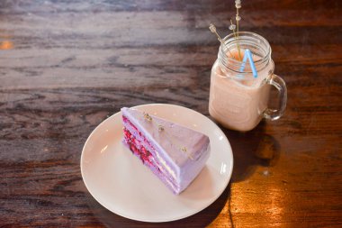 Beyaz bir tabakta lavanta çiçekleriyle servis edilen mor lavantalı kek dilimi ve koyu ahşap arka planda lavanta kahvesi. Çay için eşsiz tatlı..