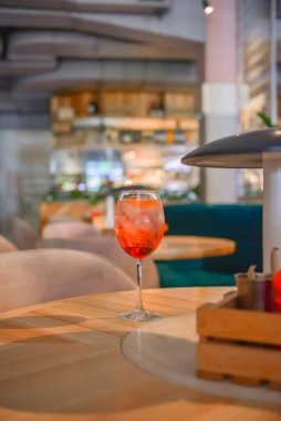 Kırmızı narenciye kokteyli. Şarap kadehinde alkollü yaz içeceği. Restoranın içindeki ahşap bir masada buzlu içecek. Konsepti tüketiyorum. Bulanık arkaplan.