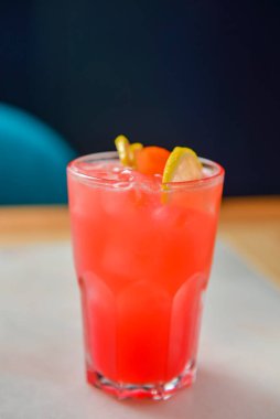 Siyah arka planda kırmızı renkli, turunçgil meyveli kokteyl. Tahta bir masada şarap kadehinde servis edilmiş. Tahta bir masada buzlu ve kirazlı alkollü yaz içeceği.