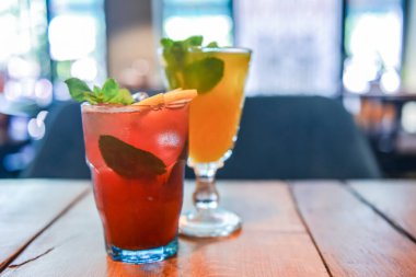 Ahşap masada iki kokteyl. Kırmızı meyve kokteyli, ahududu ve nane aromalı soğuk narenciye. Kırsal ahşap masada servis ediliyor. Bulanık restoran geçmişi.