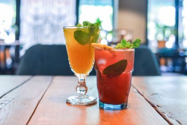 Ahşap masada iki kokteyl. Kırmızı meyve kokteyli, ahududu ve nane aromalı soğuk narenciye. Kırsal ahşap masada servis ediliyor. Bulanık restoran geçmişi.