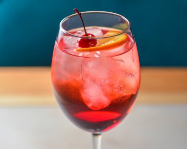 Siyah arka planda kırmızı renkli, turunçgil meyveli kokteyl. Tahta bir masada şarap kadehinde servis edilmiş. Tahta bir masada buzlu ve kirazlı alkollü yaz içeceği.