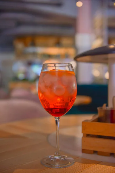 赤い柑橘系のカクテルとガラス ワイングラスでアルコール夏の飲料 レストラン内の木のテーブルの上に氷でリフレッシュドリンク コンセプトを食べる ぼやけた背景 — ストック写真