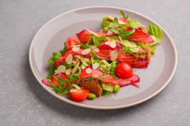 Taze salata, füme tuzlu somon, domates ve kabak çekirdeği. Gri desenli arka planda gri bir tabakta servis edilmiş. Organik lezzetli yemekler, sağlıklı yemekler..