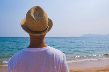 Yaz tatili, seyahat, turizm ve tatil konsepti. Okyanusa bakan plajda şapkalı bir çocuk. Mavi deniz dalgaları. Sahilde keyif çatmak ve dinlenmek. Seyahat konsepti, otel işi. Boşluk afişini kopyala.