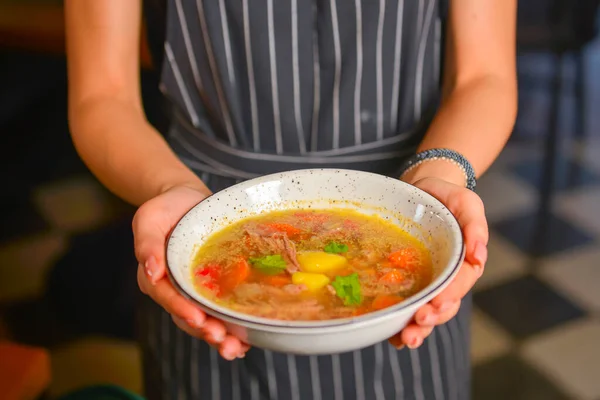 Restoranda bir kase sıcak çorba servis eden siyah üniformalı bir garson. Lezzetli ve sağlıklı bir yemek konsepti. Restoran servisi. İşte üniformalı garson..