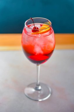 Kırmızı narenciye kokteyli. Şarap kadehinde alkollü yaz içeceği. Restoranın içindeki ahşap bir masada buzlu içecek. Konsepti tüketiyorum. Bulanık arkaplan.