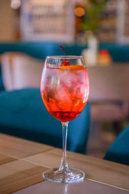 Kırmızı narenciye kokteyli. Şarap kadehinde alkollü yaz içeceği. Restoranın içindeki ahşap bir masada buzlu içecek. Konsepti tüketiyorum. Bulanık arkaplan.