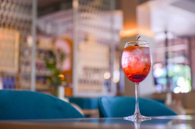 Kırmızı narenciye kokteyli. Şarap kadehinde alkollü yaz içeceği. Restoranın içindeki ahşap bir masada buzlu içecek. Konsepti tüketiyorum. Bulanık arkaplan.