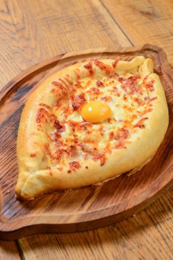Peynir ve yumurtalı Hhachapuri, ahşap bir masada servis edilen tahta bir tabakta. Geleneksel Gürcistan mutfağı, lezzetli yemekler.