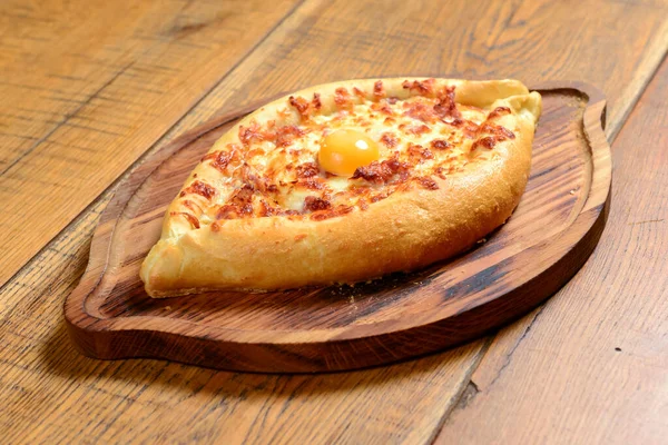 Peynir ve yumurtalı Hhachapuri, ahşap bir masada servis edilen tahta bir tabakta. Geleneksel Gürcistan mutfağı, lezzetli yemekler.