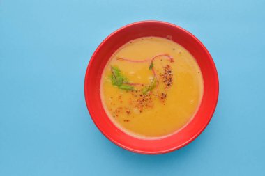 Biberiye ve biberiyeli kabak çorbası. Kırmızı kasede servis edilen kremalı çorba mavi arka planda. Lezzetli ve sağlıklı yemek konsepti. Boşluk afişini kopyala.