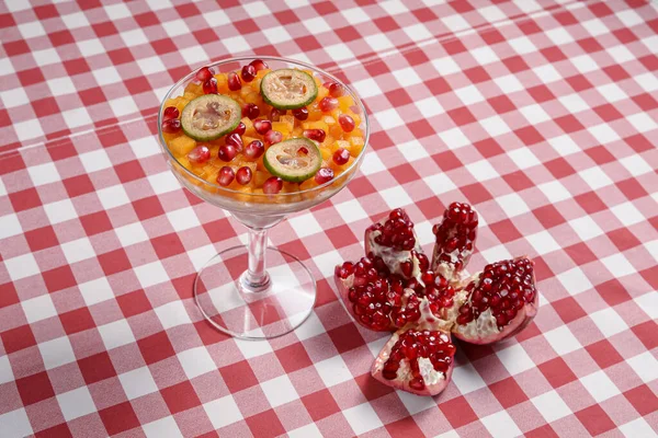Sweet dessert pannacotta with pomegranate jelly and served with pomegranate syrup and seeds in a tall glass over red plaid tablecloth. Italian concept. Fruit dessert.