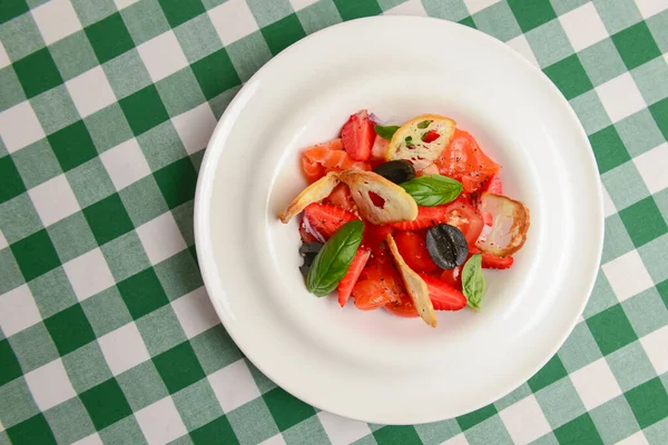 Summer salmon salad with strawberry, tomato, olives and basil in a white plate. Traditional Italian cuisine concept, delicious seasonal meal.