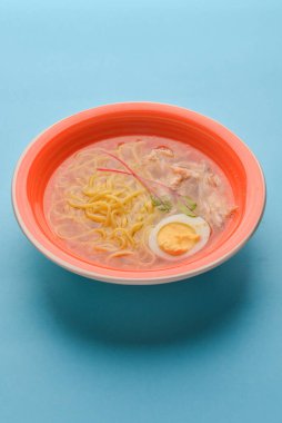 Japon ramen çorbası. Geleneksel Japon mutfağı kavramı. Lezzetli ve sağlıklı bir yemek. Pastel mavi arka planda parlak pembe bir plarw ile servis edilir..