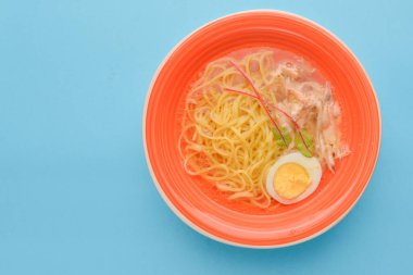 Japon ramen çorbası. Geleneksel Japon mutfağı kavramı. Lezzetli ve sağlıklı bir yemek. Pastel mavi arka planda parlak pembe bir plarw ile servis edilir..