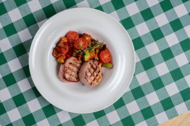 Taze et ve sebze ızgarada hazır. Et ve sebzeler. Mevsimlik yaz yemeği konsepti, barbekü konsepti. Yeşil ekose masa örtüsünün üzerinde beyaz bir tabakta servis ediliyor..