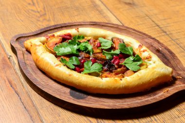 Ahşap kesme tahtasının ortasını et ve taze yeşillikle dolduran geleneksel Adjarian Khachapuri şeklinde bir tekne. Gürcistan mutfağı kavramı.