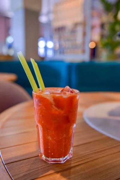 Piros koktél jéggel, üvegben tálalva, fából készült asztalon, homályos éttermi háttérrel. Frissítő nyári ital. — Stock Fotó