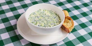 Popüler bahar ya da yaz soğuk çorbası okroshka. Okroshka beyaz kasede, ekmek ve otlar masada. Rus, Ukraynalı ve Gürcü mutfağı.