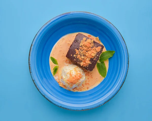 Hot fudge sundae vanilla ice cream with a hot chocolate brownie cake in a blue bowl over pastel blue background. Delicious summer chocolate dessert for tea or coffee.