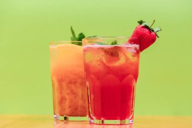 Meyve suyu ve buzlu yaz içecekleri. Yeşil arka plan ve ahşap masa üzerinde farklı bardaklarda yaz içeceklerini tazelemek. Alkol içecekleri konsepti.