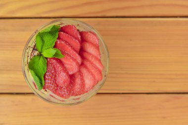 Cam kavanozda meyveli ve krem peynirli katmanlı tatlı, seçici odaklanma. Küçük bir bardakta, ahşap zemin üzerinde çilekli süt tatlısı. Dışarıda, lokanta konseptinde yemek yiyoruz..