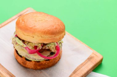 Ahşap tepside beyaz masa örtüsü ve parlak yeşil arka planda ev yapımı hamburger. Abur cubur, fast food konsepti. Lezzetli sulu burger..