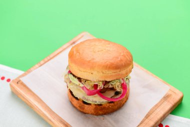 Ahşap tepside beyaz masa örtüsü ve parlak yeşil arka planda ev yapımı hamburger. Abur cubur, fast food konsepti. Lezzetli sulu burger..