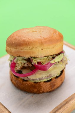 Ahşap tepside beyaz masa örtüsü ve parlak yeşil arka planda ev yapımı hamburger. Abur cubur, fast food konsepti. Lezzetli sulu burger..