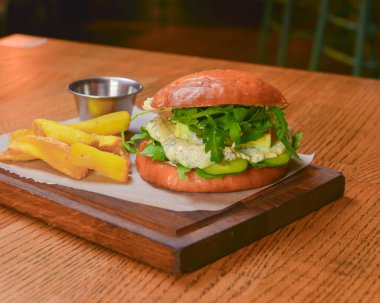 Lezzetli, sulu şef çizburgerin yanında patates kızartması var. Barda ya da restoranda masanın üstünde. Seçici odaklanma, bulanık arkaplan. Abur cubur, fast food konsepti.