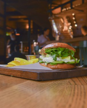 Lezzetli, sulu şef çizburgerin yanında patates kızartması var. Barda ya da restoranda masanın üstünde. Seçici odaklanma, bulanık arkaplan. Abur cubur, fast food konsepti.