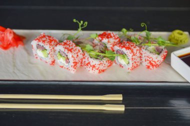 Somon ve havyarlı suşi ruloları bir restoranda ahşap bir masada geleneksel bir tabakta servis edilir. California ya da Philadelphia suşi seti zencefil ve wasabi sosuyla servis edilir. Geleneksel Japon mutfağı.