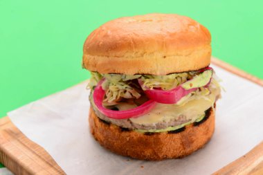 Ahşap tepside beyaz masa örtüsü ve parlak yeşil arka planda ev yapımı hamburger. Abur cubur, fast food konsepti. Lezzetli sulu burger..