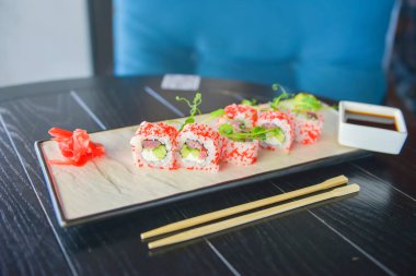 Somon ve havyarlı suşi ruloları bir restoranda ahşap bir masada geleneksel bir tabakta servis edilir. California ya da Philadelphia suşi seti zencefil ve wasabi sosuyla servis edilir. Geleneksel Japon mutfağı.