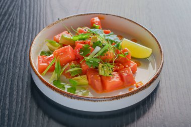 Fettalı karpuz salatası, taze yeşillik ve limon siyah ahşap masanın üzerinde eşsiz şekilli bir tabakta servis edilir. Lezzetli yaz salatası. Lezzetli yemek konsepti..