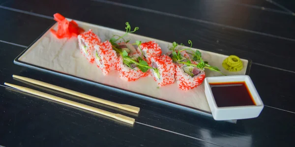 鮭とキャビアの寿司ロールは レストランの木製のテーブルの上に伝統的なプレート上で提供しています カリフォルニアやフィラデルフィアの寿司セットには生姜とわさびソースが添えられている 日本の伝統料理 — ストック写真