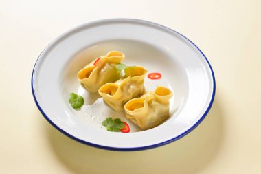 Düz beyaz tabakta servis edilen sıcak buharlı haşlanmış hamur köfteleri. Parlak yeşil arka planda Asya yemekleri.