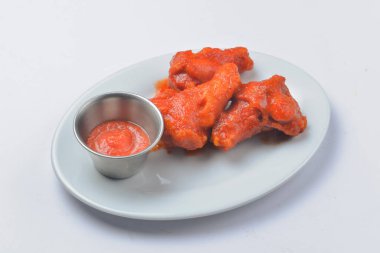 Domates soslu tavuk kanadı. Beyaz arka planda beyaz bir tabakta servis edilmiş. Kapatın. Fast food, abur cubur kavramı.