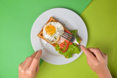 Tabakta kızarmış yumurta ve sebzeli ekşi waffle. Lezzetli geleneksel kahvaltı fikri. Viyana waffle 'ı, Belçika waffle tarifi. Çatal ve bıçaklı yeşil arka plan elleri, ye. Boşluk afişini kopyala.