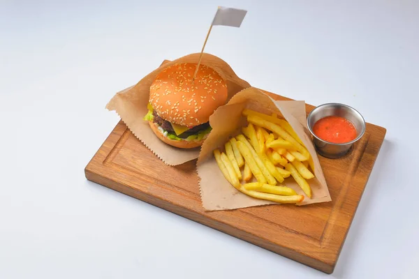 Patates kızartması ve domates soslu hamburger. Fast food, abur cubur konsepti. Beyaz arka planda, ahşap bir tahtanın üzerinde servis edilmiş. Kapat..