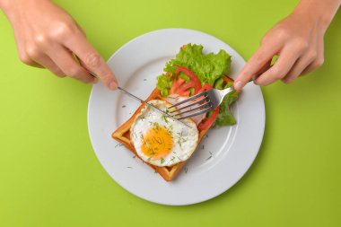 Tabakta kızarmış yumurta ve sebzeli ekşi waffle. Lezzetli geleneksel kahvaltı fikri. Viyana waffle 'ı, Belçika waffle tarifi. Çatal ve bıçaklı yeşil arka plan elleri, ye. Boşluk afişini kopyala.