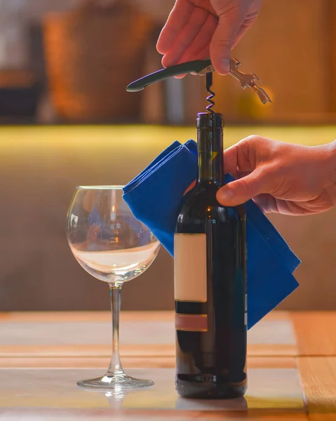 Wine glass and bottle of red wine on a wooden table over blurred background. Restaurant service, eating out concept. Drinking alcohol in a restaurant, celebration. Man, waiter opens a bottle of wine.