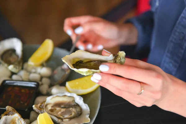 Fresh oysters as well as fine dining, young attractive woman eating oysters in restaurant. Eating out concept, dinner in restaurant.