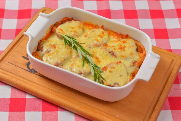 Zucchini baked with cheese in a dish, close up food. Delicious meat and cheese casserole. Italian cuisine concept, green plaid table cloth.