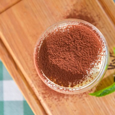 Bulanık restoran arka planında servis edilen bir bardakta tiramisu keki. İtalyan mutfağı konsepti, geleneksel yeşil masa örtüsü..