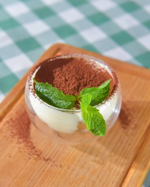 Bulanık restoran arka planında servis edilen bir bardakta tiramisu keki. İtalyan mutfağı konsepti, geleneksel yeşil masa örtüsü..